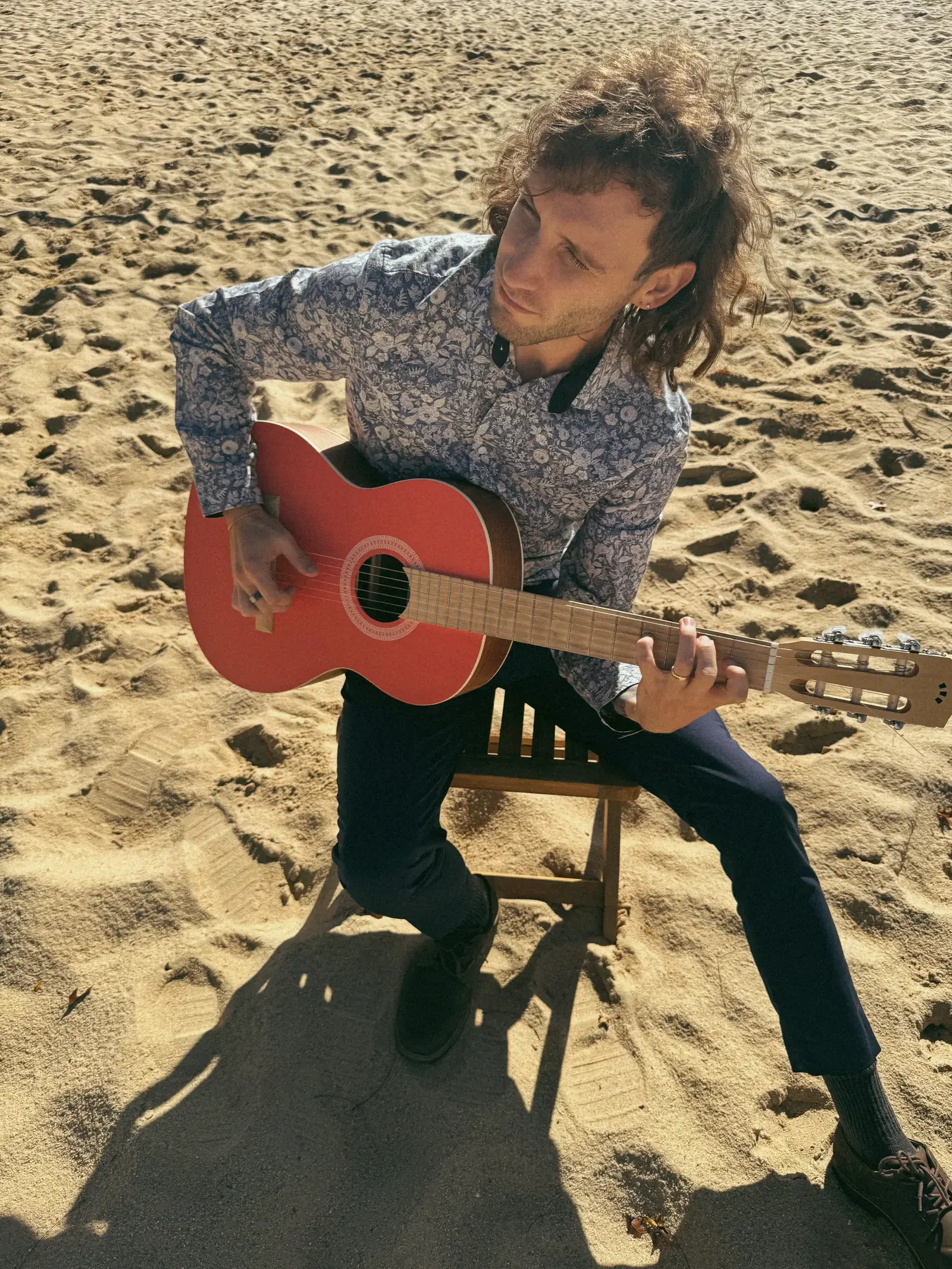 Mathew looking up while playing guitar on a sandy path.