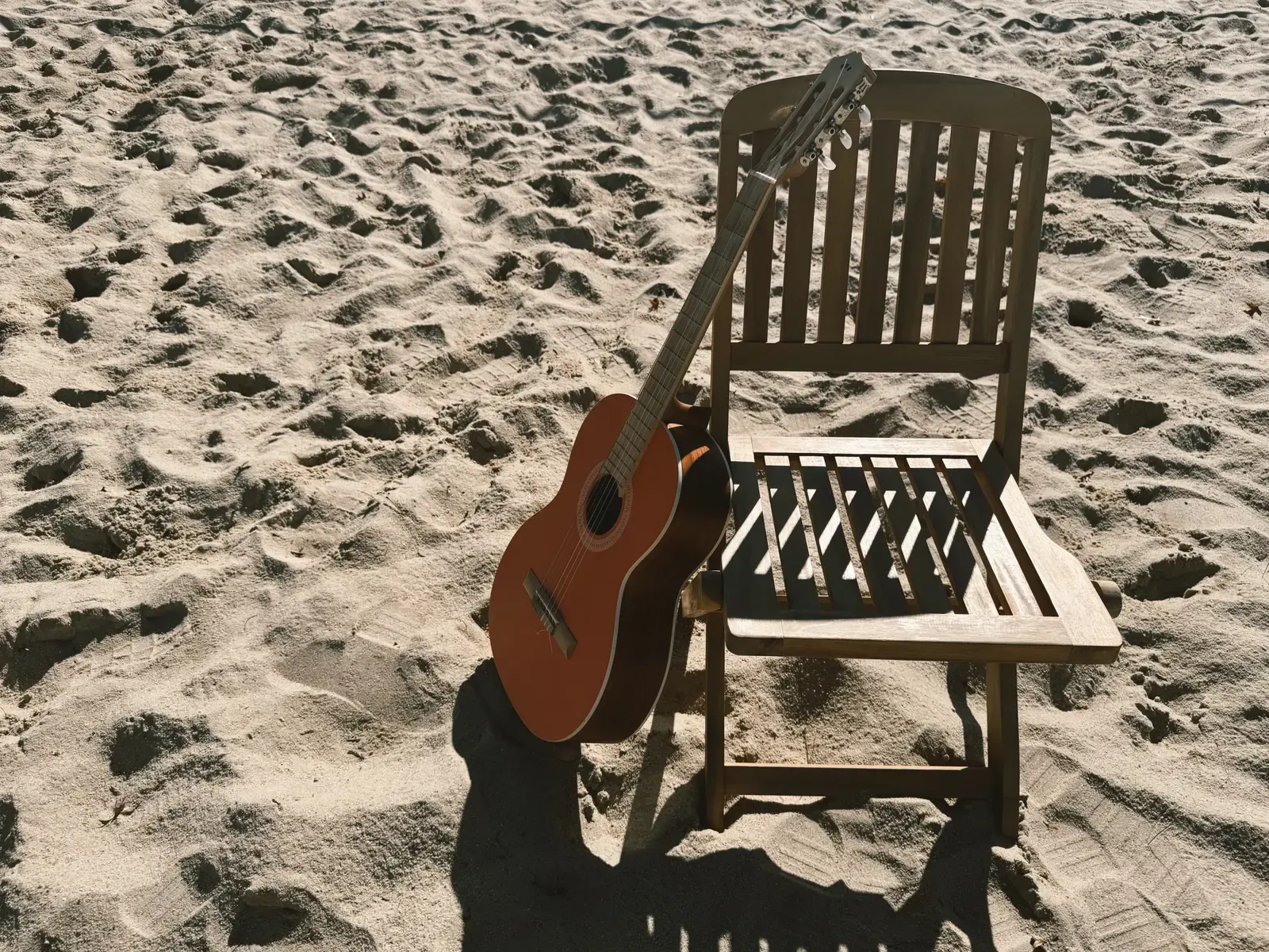 Mathew’s orange-red guitar resting against a wooden chair in sunlight.
